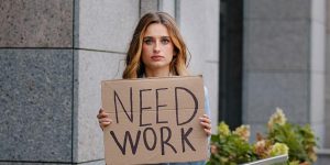 unemployed-woman-holds-a-sign-that-says-need-work.jpg